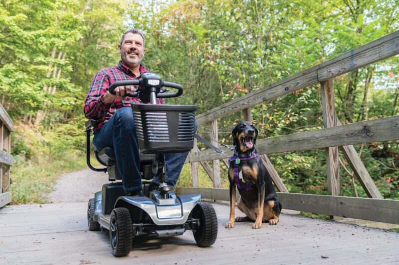 Middle-aged man on scooter crossing bridge with dog on leash